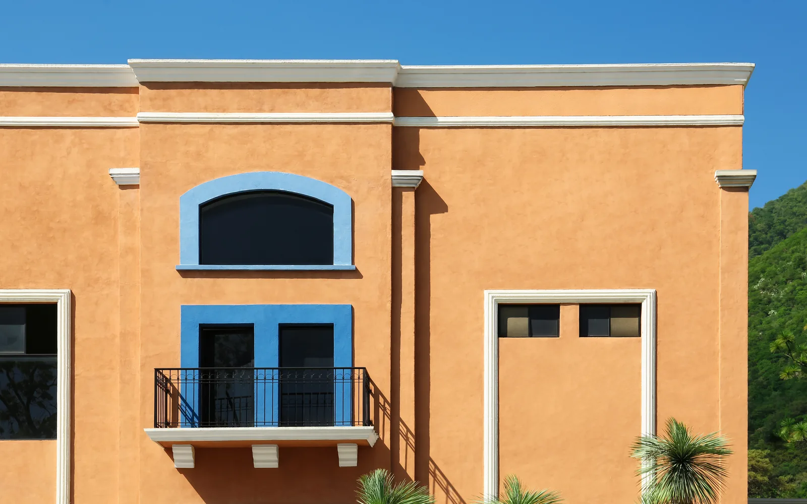 Orange stucco commercial building with a blue-trimmed arched window and balcony