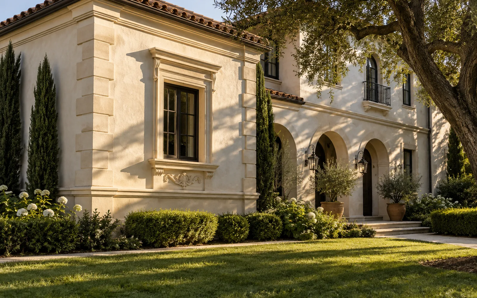 Cream stucco home with ornamental window surrounds behind a lawn