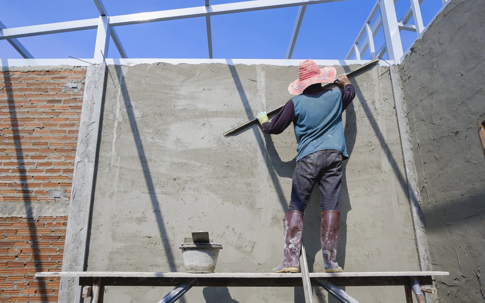 Worker plastering a wall from a scaffold platform against a blue sky
