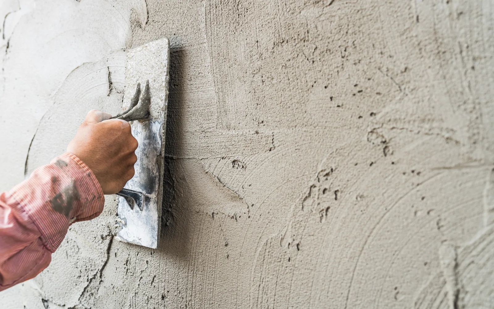 Gloved hand drawing a trowel of plaster across a textured wall
