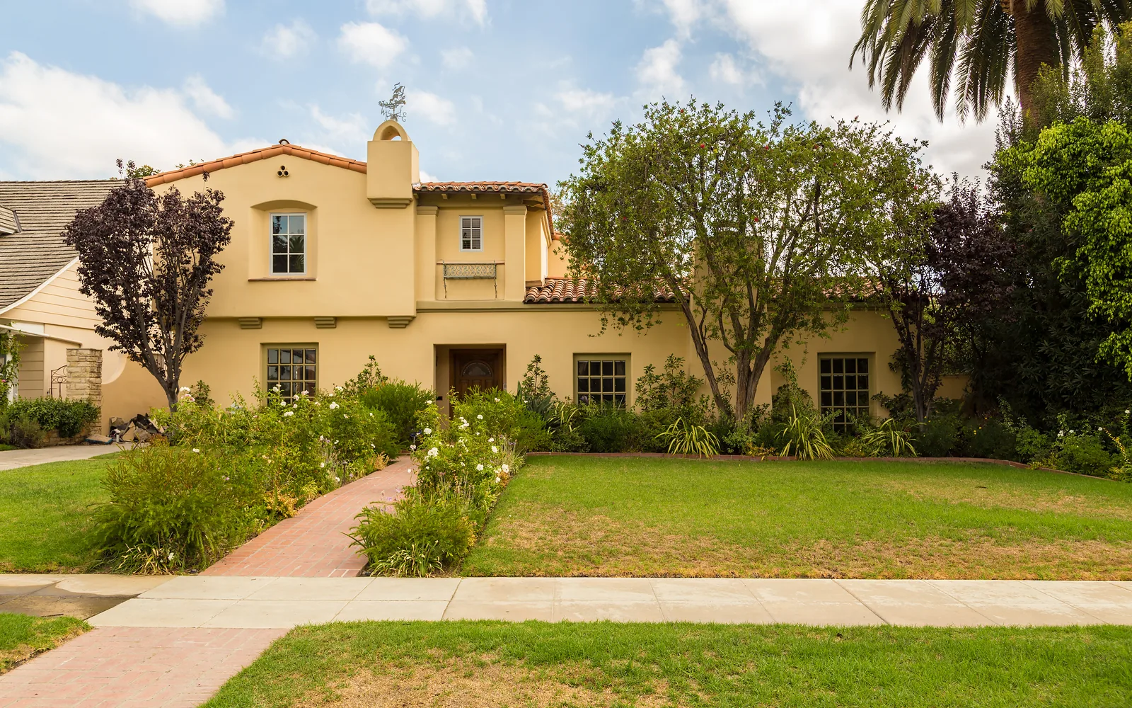 Pale yellow Spanish-style stucco home behind a lawn and front path