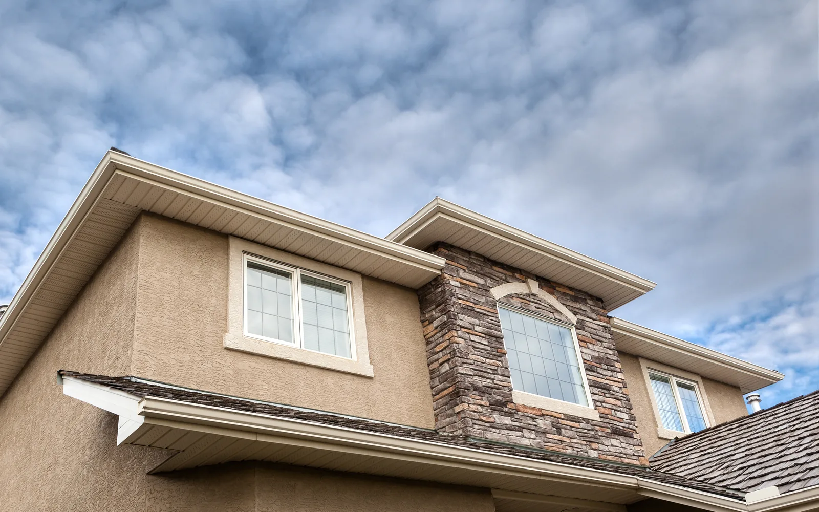 Two-storey stucco home with a stone-faced gable under cloud