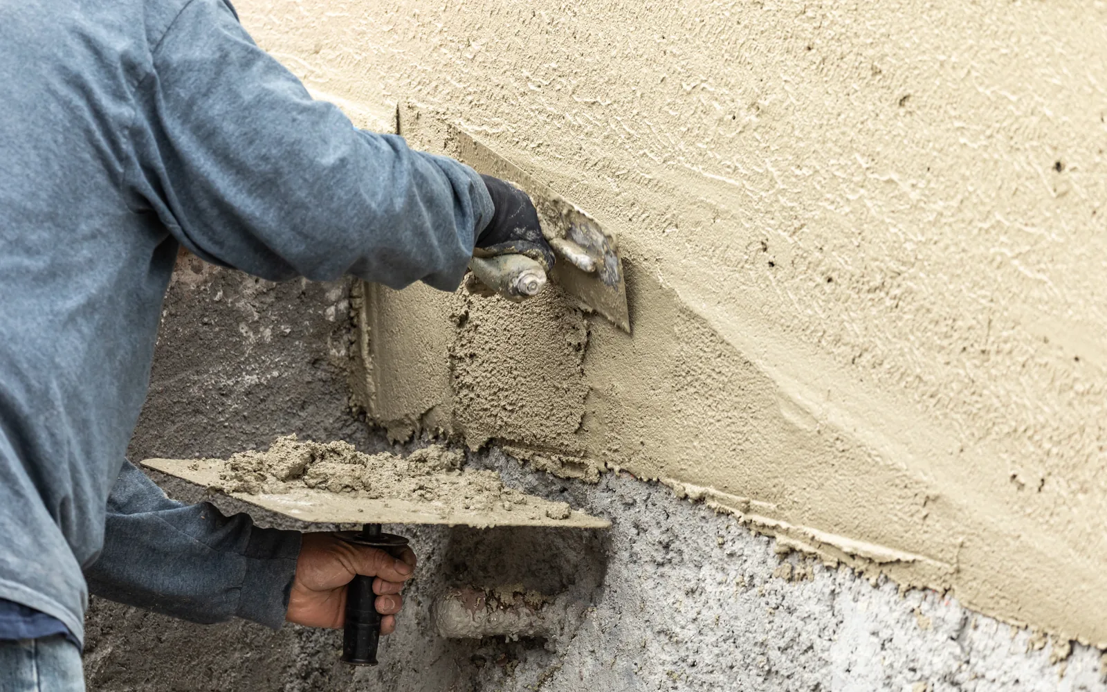 Worker cutting away failed stucco at the base of a wall