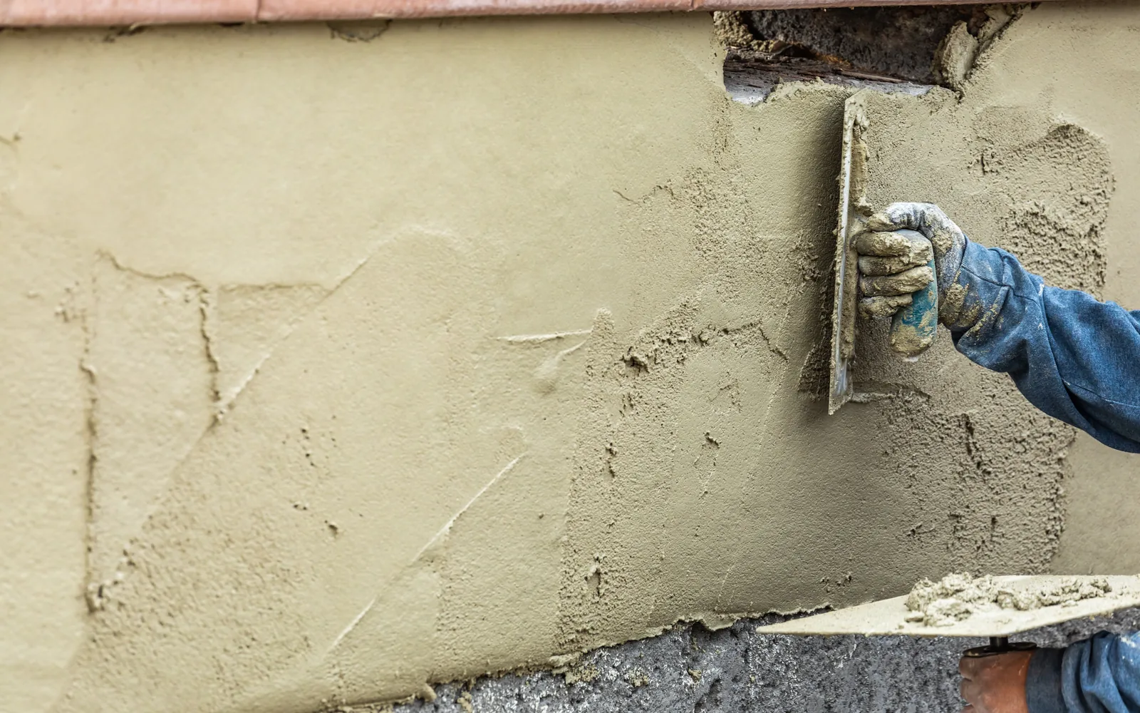 Gloved hand troweling a patch onto an olive-toned stucco wall